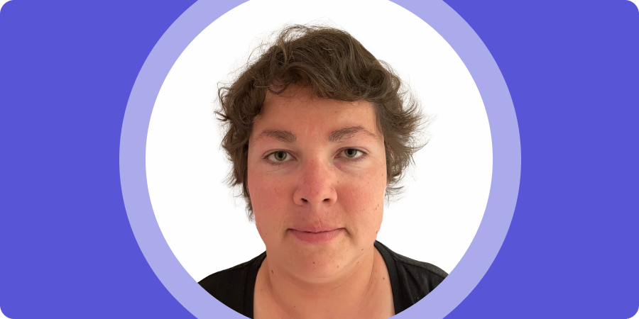 Banner image. Portrait of Kyrby B, a woman with short, wavy brown hair, wearing a black top and facing directly at the camera smiling, set inside a purple circular frame with a purple border.